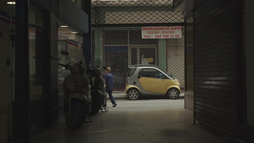 A person walks past a parked smart car in a narrow alleyway