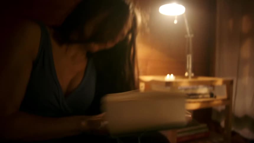 A frustrated woman tears the pages of a notebook sitting on a bed