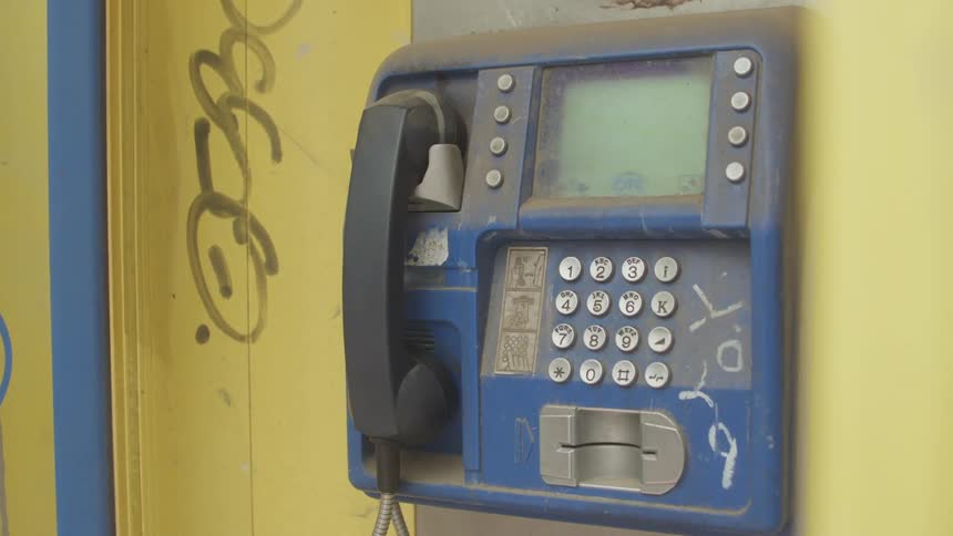 A vintage payphone hangs on a weathered yellow wall partially obscured by dust and graffiti