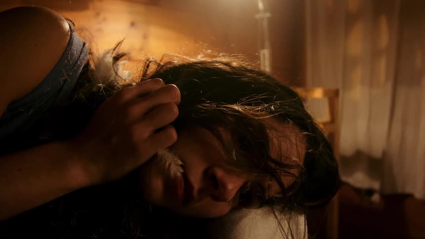 A woman rests uneasily on a bed her face showing sadness