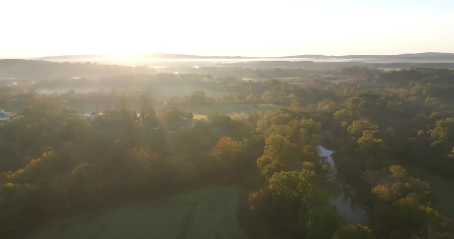 Aerial panorama of a forested area with a river and the sunrise on the horizon