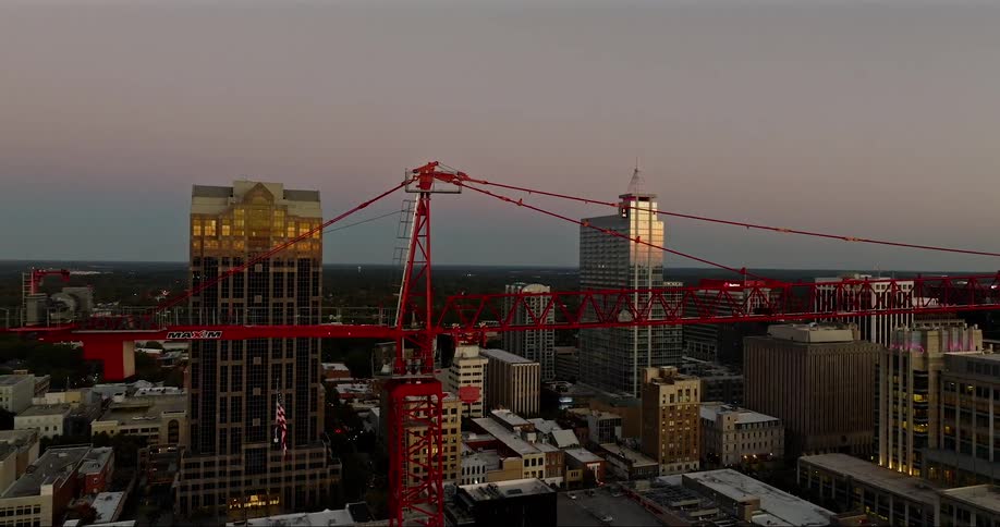 A red construction crane stands tall over a city skyline at sunset