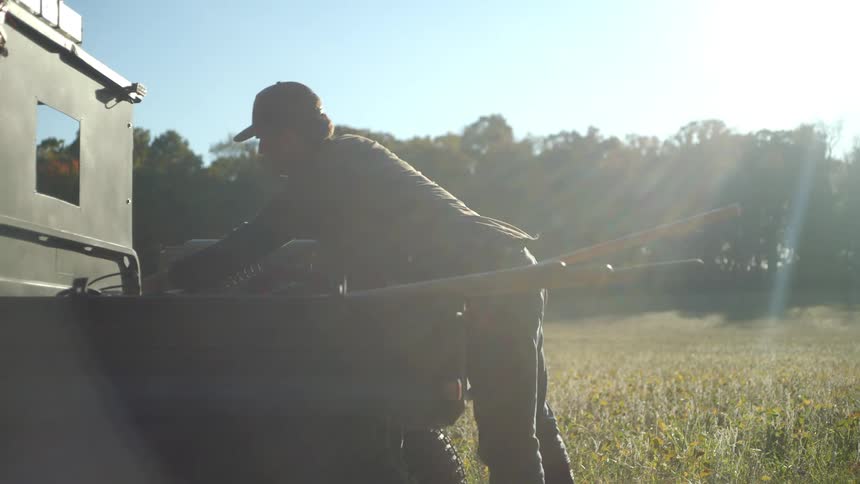 A man unloading tools from the back of a small truck in the countryside