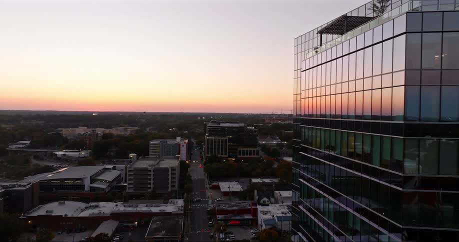 A modern skyscraper reflects the setting sun against the backdrop of a city skyline