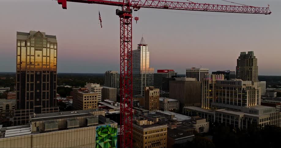 Construction crane towers over high rise and mid rise urban buildings at sunset