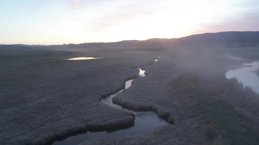 Aerial view of a river winding through a vegetation area with mountains in the background