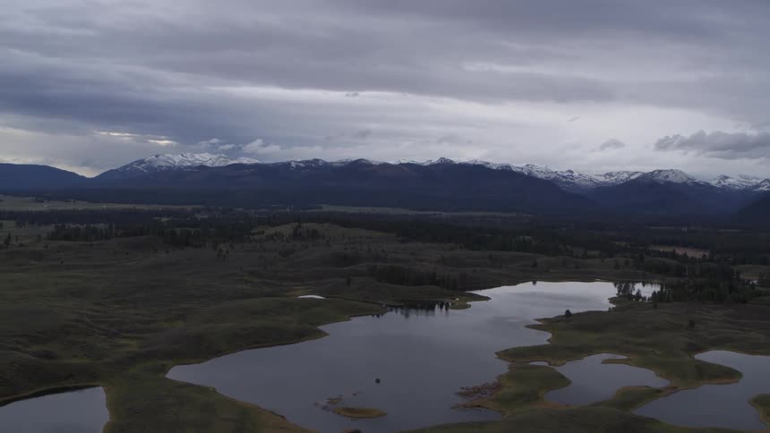 Landscape with partially snowcovered mountains in the background reflected in a large body of water surrounded by grassy areas