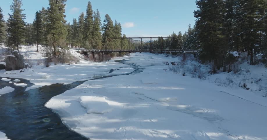 A bridge crosses a snowcovered river on a mostly sunny day