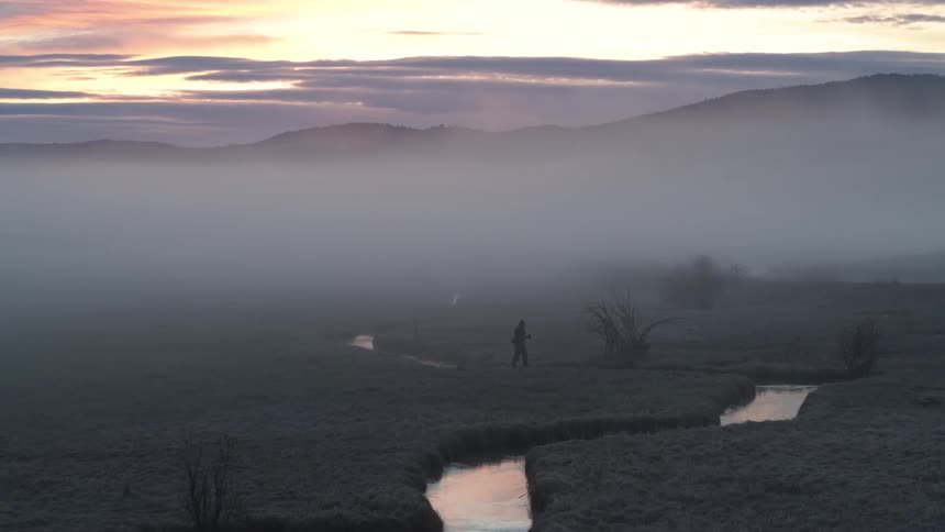 Person walking near a river on a day with low fog one morning