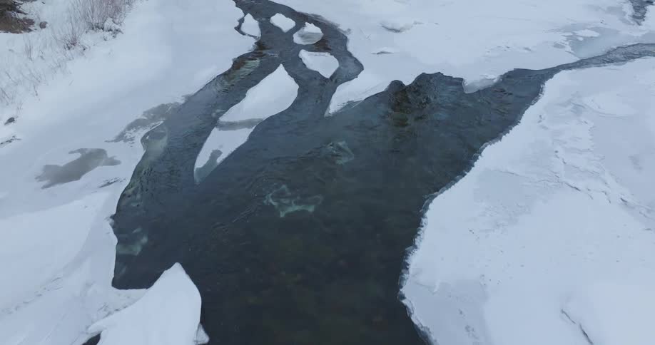 A winding river flows through a frozen landscape creating a dark winding path through the ice