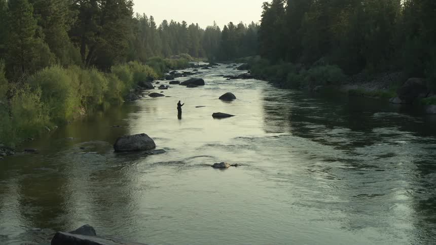 Silhouette of fisherman fly fishing in a river bed in the wilderness