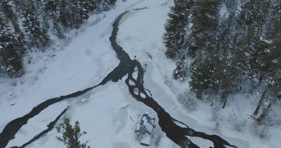 The winding river carves a dark path through the snowcovered landscape surrounded by a dense forest of evergreens