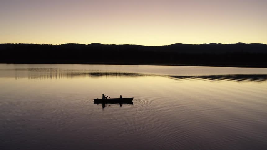Two people canoe on a still lake at dusk with mountains in the distance