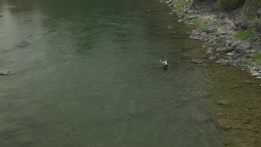 Man fishing while waistdeep in the river near the forest