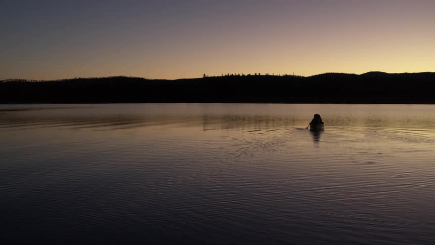 A lone canoeist paddles across a still lake at dusk