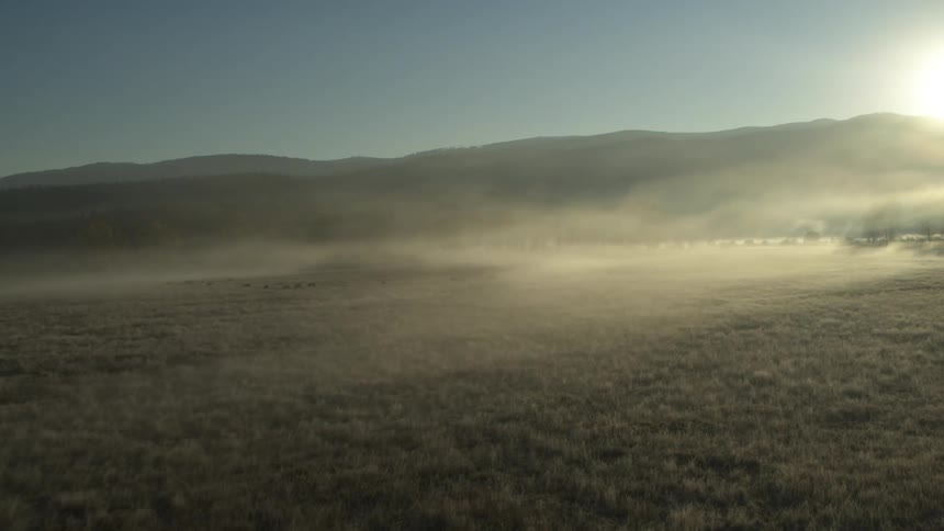 A very bright sun shines on a flat grassy field with a mountain at the end of it
