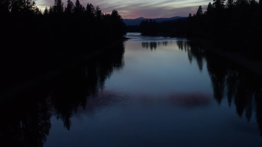 A tranquil river reflects the hues of a twilight sky framed by silhouetted trees