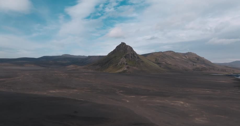 A sharp jagged mountain peak rises above a vast barren landscape under a blue sky