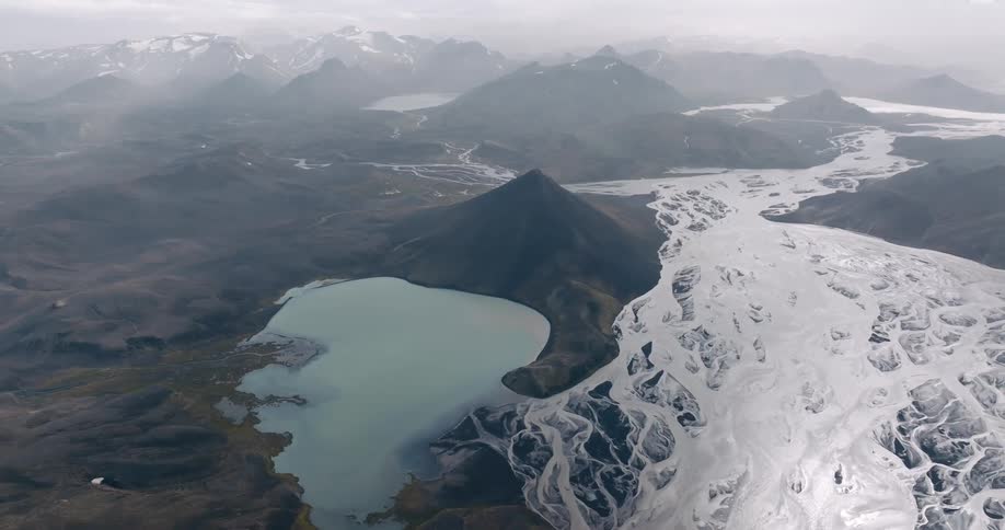 A winding river flows through a vast landscape surrounded by snowcapped mountains