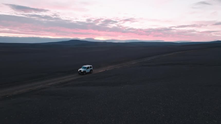 A lone vehicle journeys across a vast barren landscape under a vibrant sunset sky