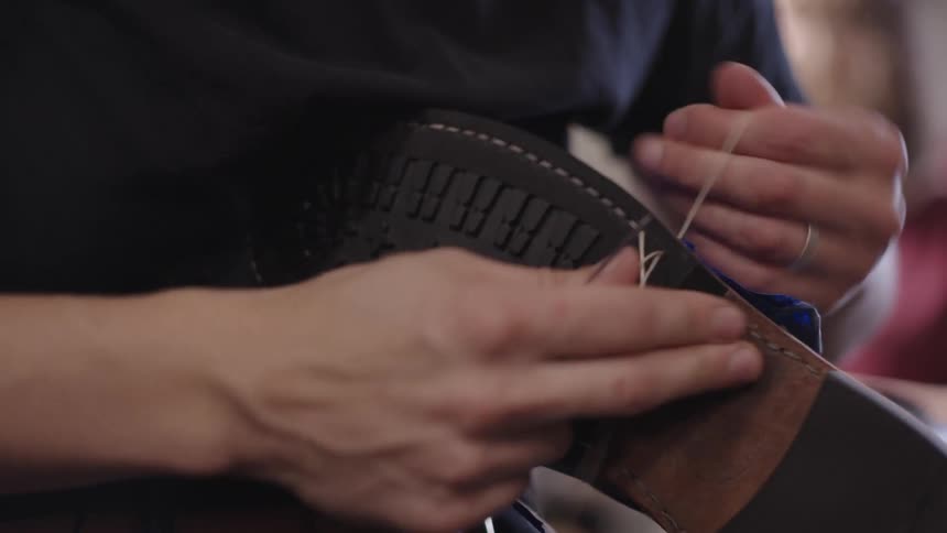 A person handstitches a leather shoe