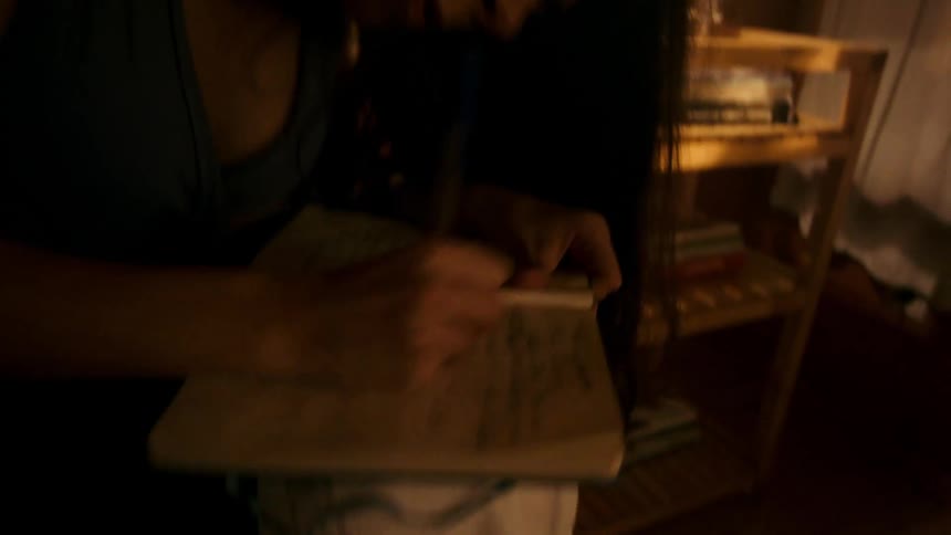 A frustrated woman scribbles furiously in a notebook sitting on a bed