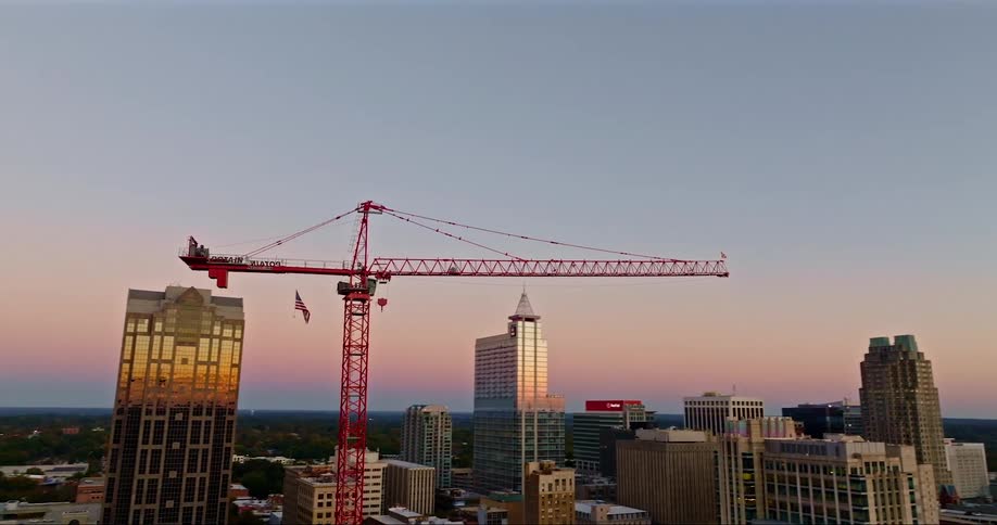 A red construction crane stands tall over a city skyline at sunset