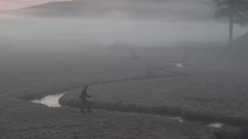 Man walking along the edge of a winding river in a land with vegetation
