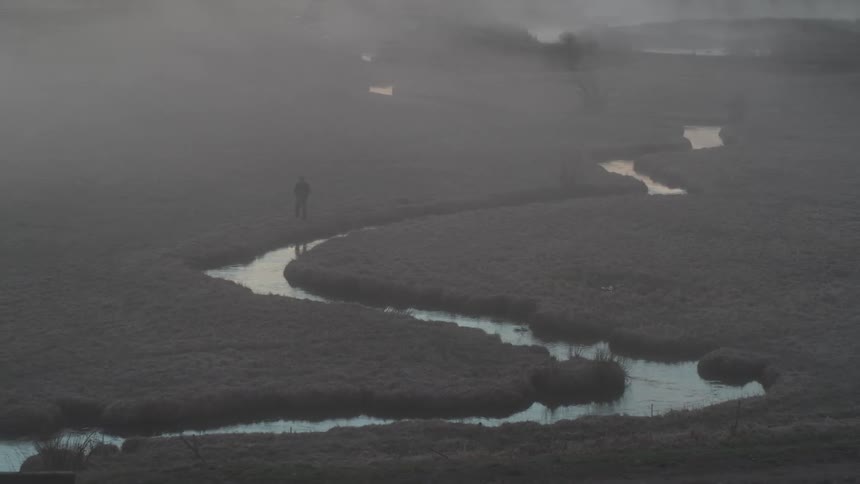 Misty landscape with a winding stream cutting through a grassy terrain