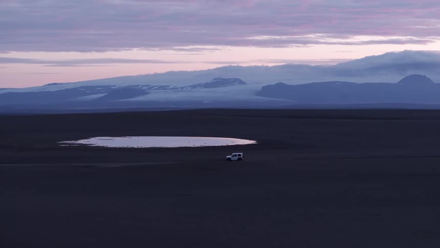 Jeep drives on a dirt road with mountains far in the distance at sunset
