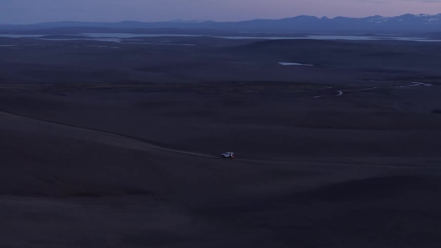 A lone vehicle journeys across the vast dark plain under a sky painted with the soft hues of twilight