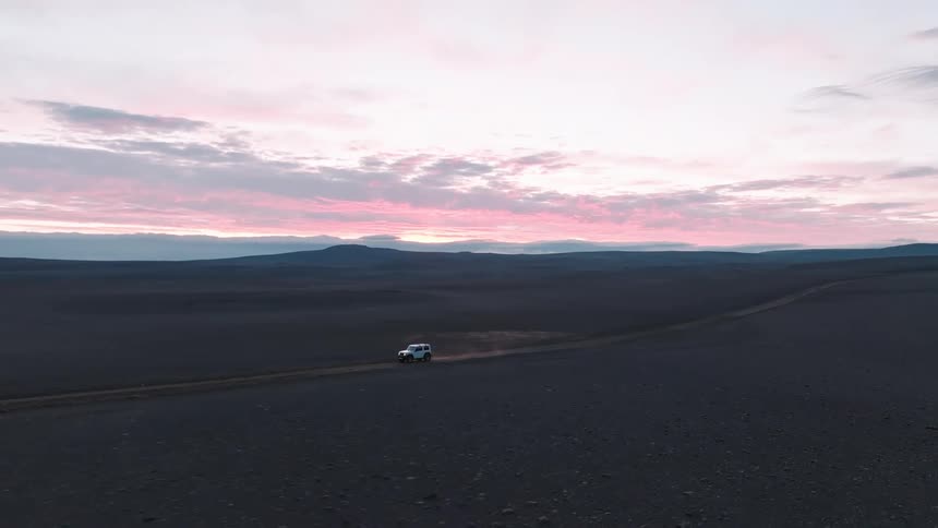 A lone vehicle journeys across the vast desolate landscape silhouetted against the vibrant hues of the sunrise
