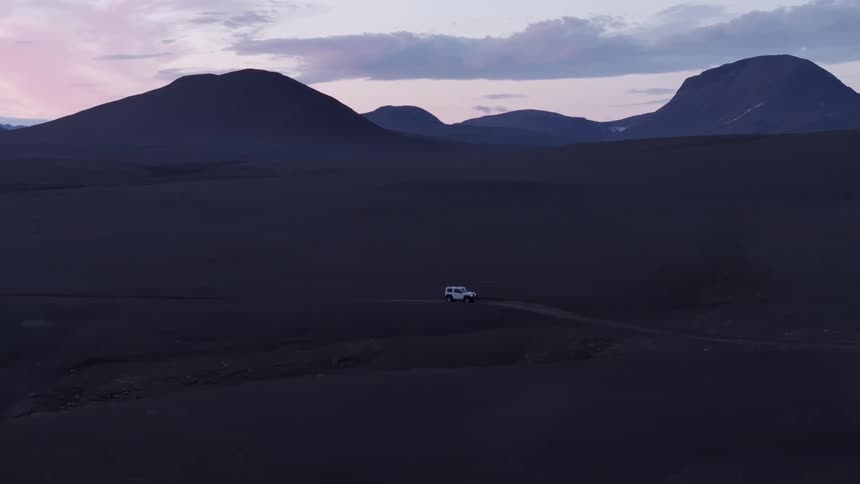 A lone vehicle traverses a vast barren landscape under a dramatic twilight sky