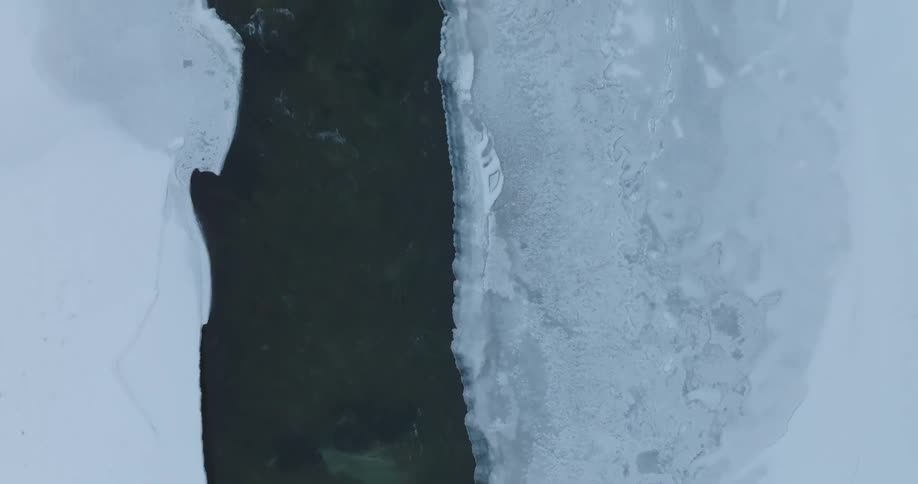 A dark river cuts through a frozen landscape surrounded by ice