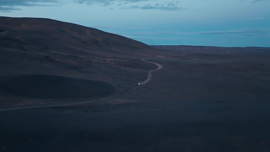 Aerial view of a car traveling along a road in a mountainous environment