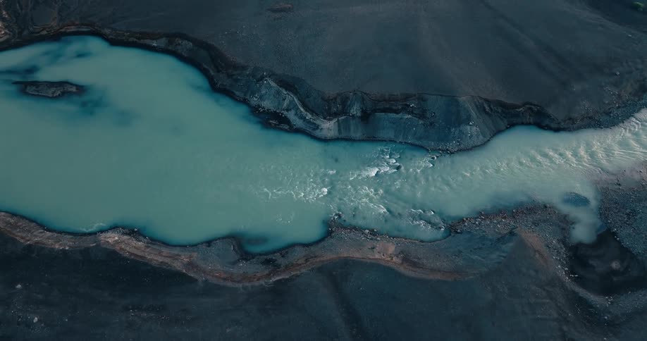 Panorama of a whitish river flowing through dense dark terrain