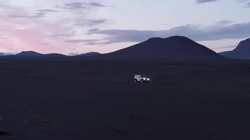 A lone vehicle traverses a desolate volcanic landscape under a twilight sky