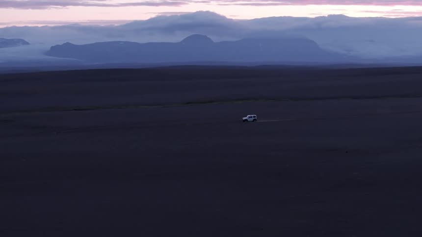 A lone vehicle traverses a vast barren landscape under a twilight sky