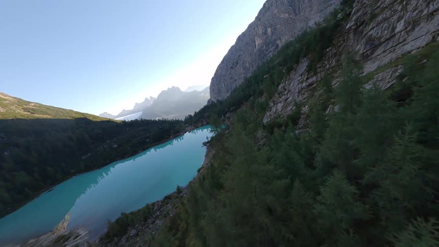 Barren path leading to a lake in front of a forested mountain under a clear blue sky