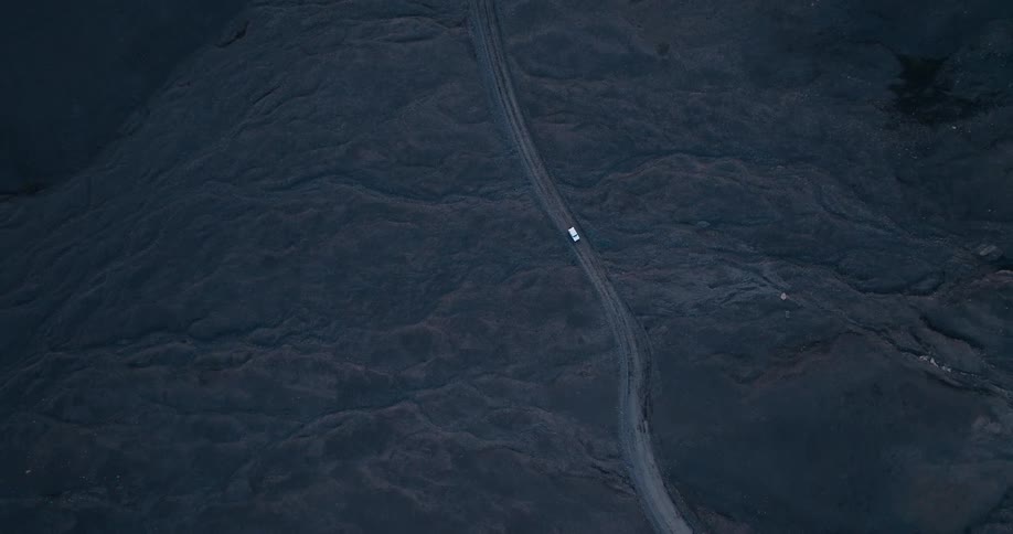 An aerial clip of a car in a black sand desert