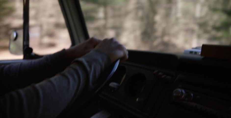 A person is gripping the steering wheel of a moving car during the daytime