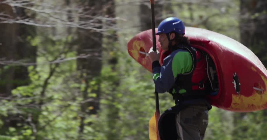 Man carrying his kayak through a wooded area
