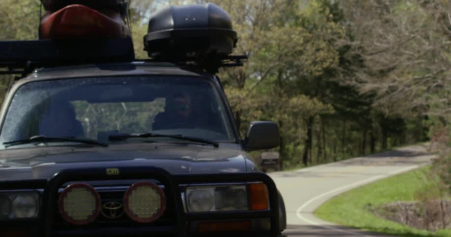 Vehicle driving down a paved road with a lot of equipment strapped to its top