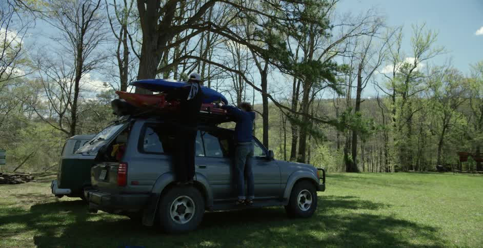 Two people are securing kayaks to the top of an suv