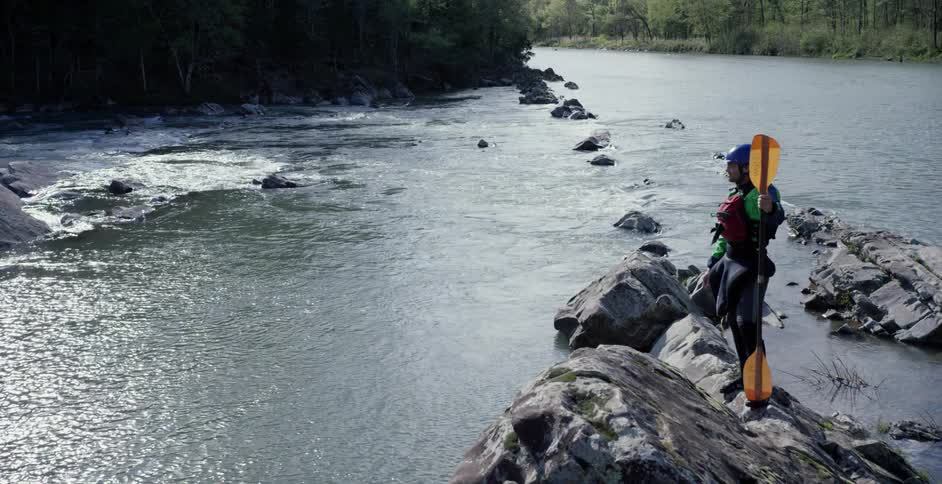 A kayaker stands on a boulder with a paddle