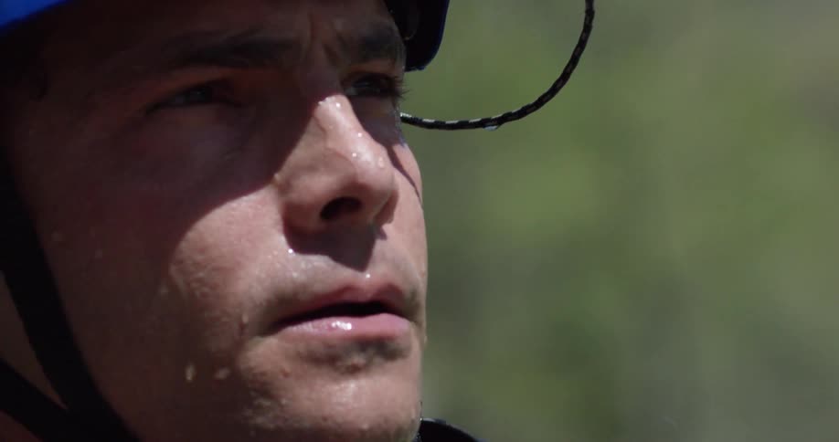 A man with a wet face is blowing water off his lips as he stands outside