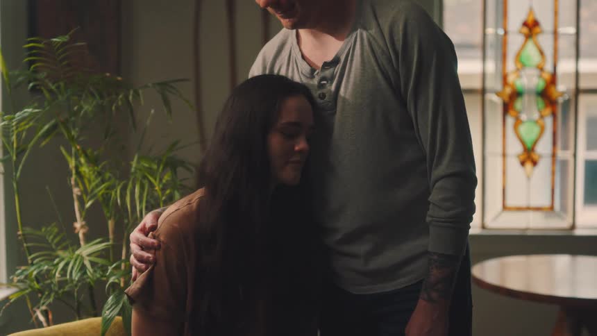 Man leans down slightly to hug a woman sitting near a stained glass window
