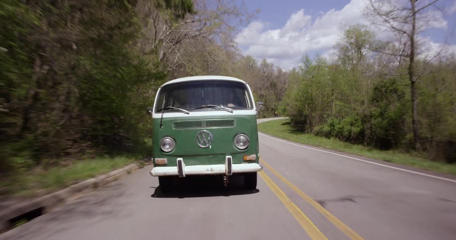 A volkswagen van drives through a forested area