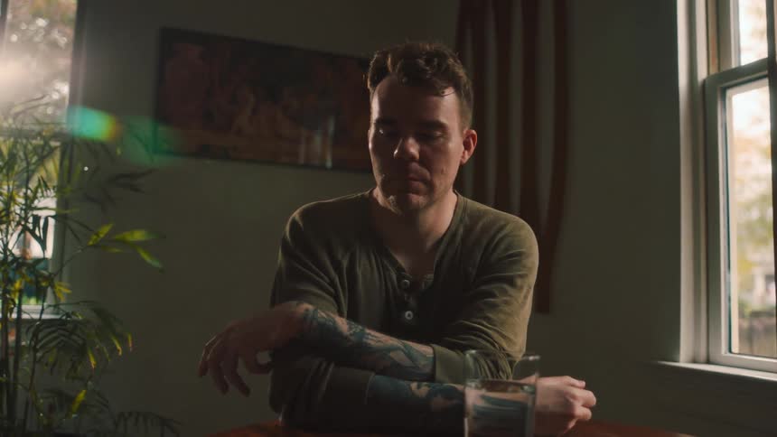 Man sitting at the table with a glass of water and looking discouraged putting his hands to his face