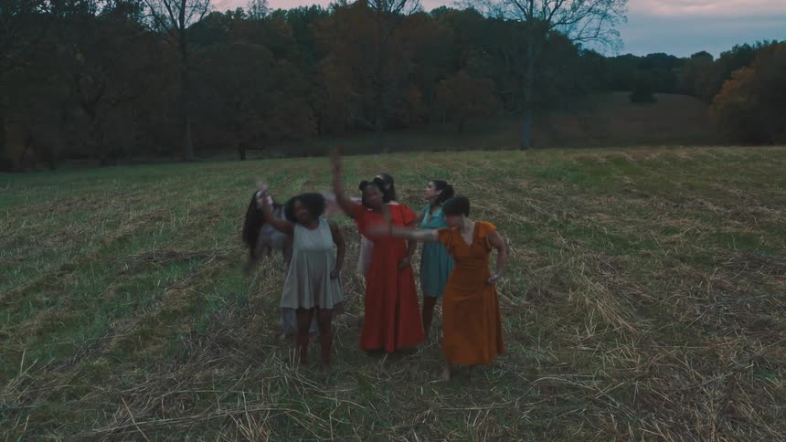 Women wearing dresses of different colors hug each other and then start dancing